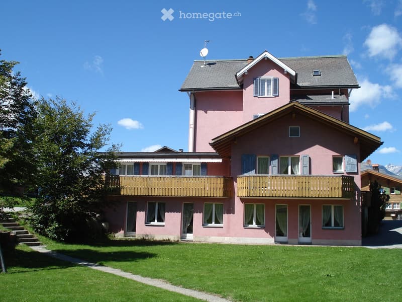 3 story house, pink exterior, wooden balconies, windows with white curtains, satellite dish on roof