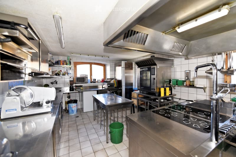 Commercial kitchen with stainless steel countertops, industrial appliances, and a tiled floor.