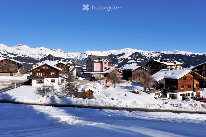 Traditional wooden chalets, snow-covered roofs, surrounded by snow-covered mountains, clear blue sky