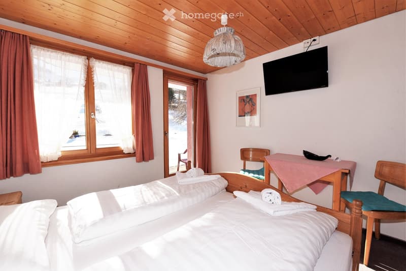 bedroom with two beds, wooden ceiling, white walls, large windows, TV, table, chairs, towels