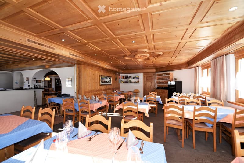 Wooden ceiling, wooden walls, tables and chairs, wine glasses, cutlery, counter, shelves, windows