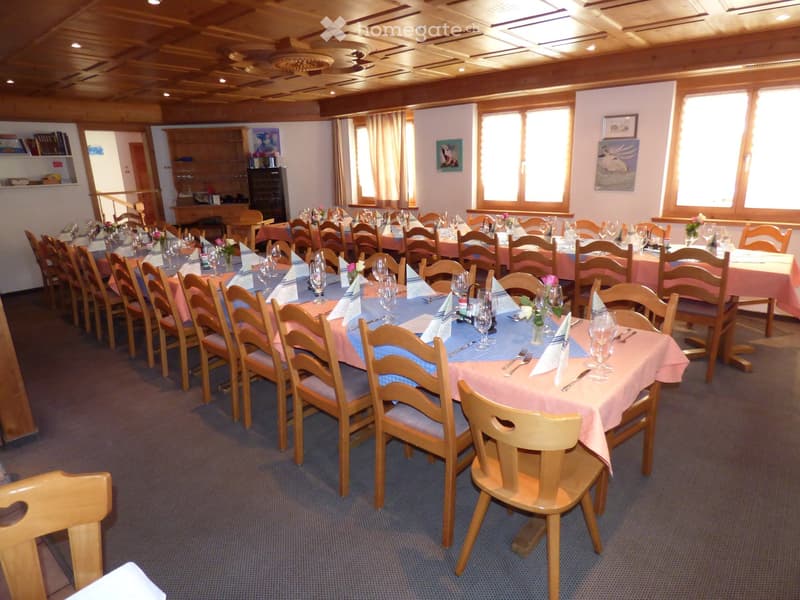 Dining room with long tables, wooden chairs, pink tablecloths, wine glasses, and flower arrangements