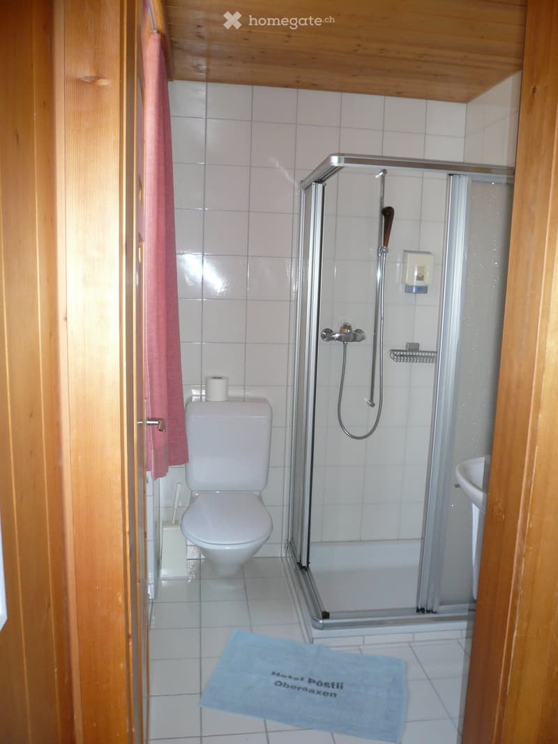 white tiled walls, white toilet, glass shower enclosure, white sink, towel, wooden door