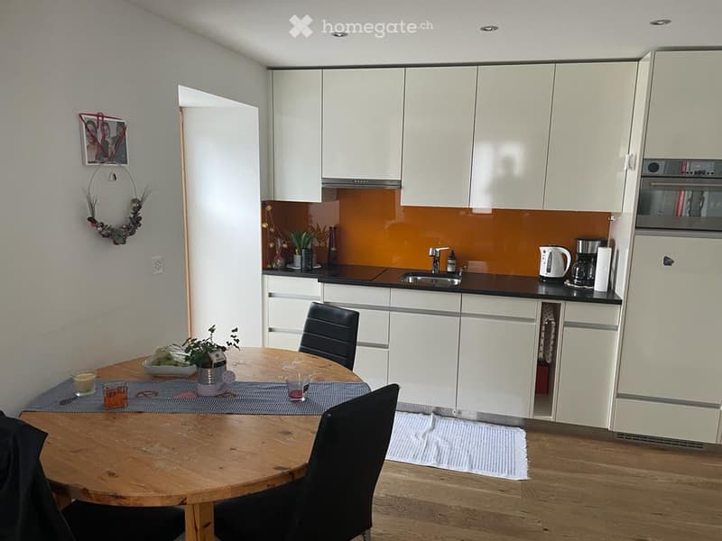 modern kitchen with white cabinets, wooden floor, round dining table, black chairs, sink, stove, refrigerator, microwave, coffee maker, kettle, and decorative items