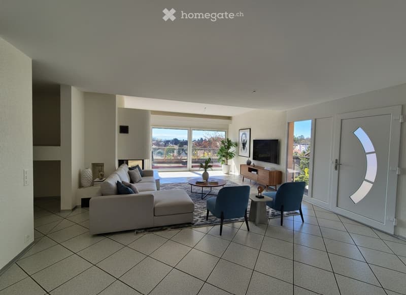 Modern living room with large windows offering a view, a grey sectional sofa, coffee table, armchairs, ottoman, TV, and decorative items.
