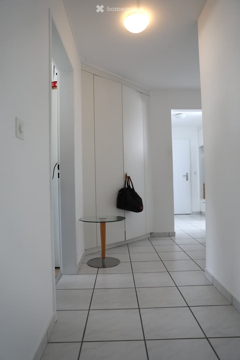 Empty room with white walls, white tile floor, glass table, white cabinets, black bag hanging on the wall, light on the ceiling