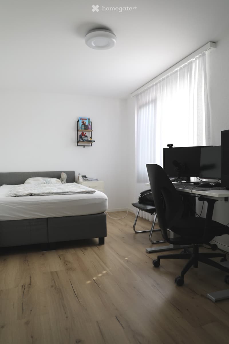 Bedroom with bed, desk, chair, monitors, keyboard, mouse, shelves, lamp, and window with curtains