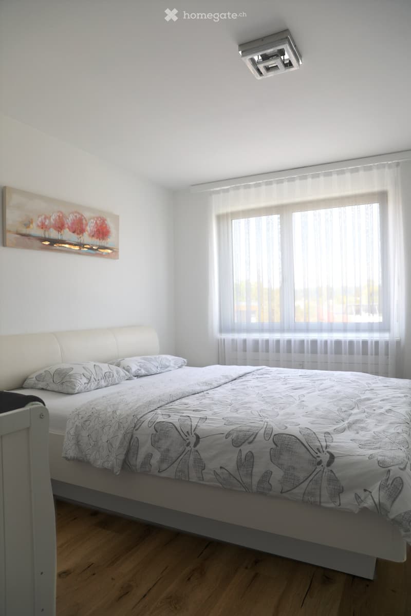 white walls, wooden floor, large bed, white curtains, painting on wall, ceiling light