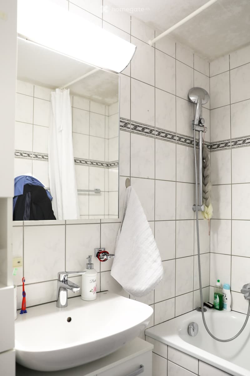 white tiles, white sink, mirror, bathtub, shower, towel, toiletries