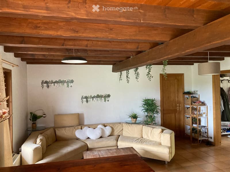 L-shaped beige sofa, wooden coffee table, wooden beams, white walls, plants, lamps