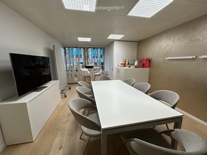 modern meeting room with a long white table, gray chairs, a flat screen TV, and a white cabinet