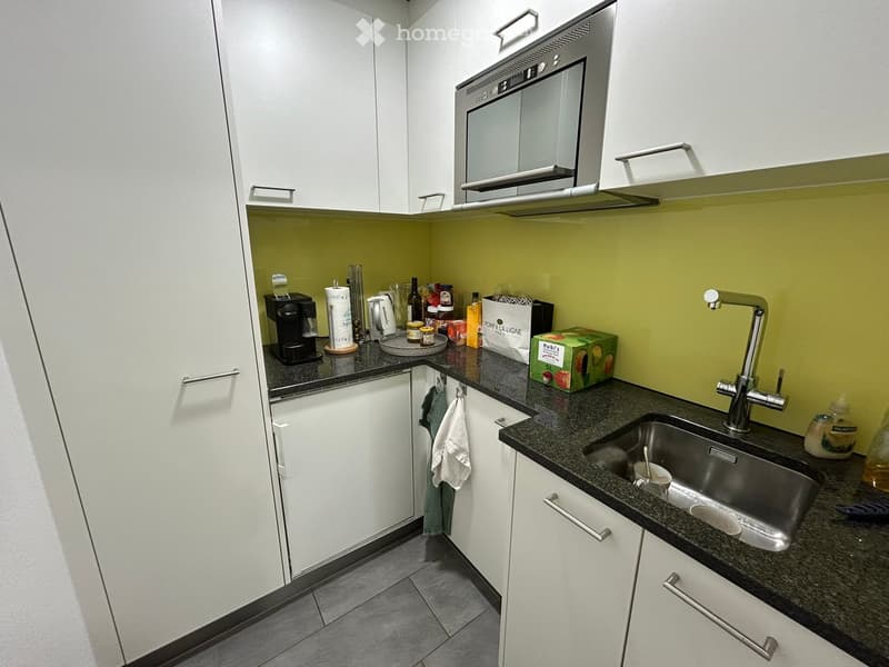 modern kitchen with white cabinets, granite countertops, stainless steel sink, built-in microwave, dishwasher, coffee machine, and various kitchen items