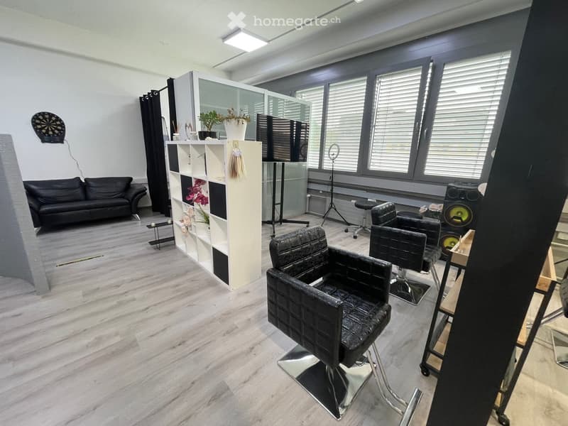 Interior of a salon with black leather chairs, a white shelf, a black couch, a dartboard, and a black stool.