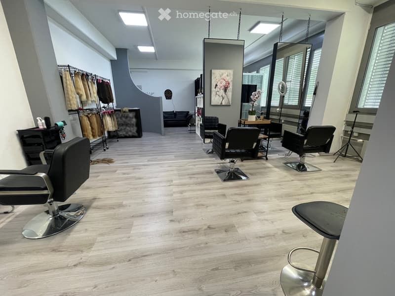 Hair salon with wooden floor, black chairs, mirrors, and a table with flowers