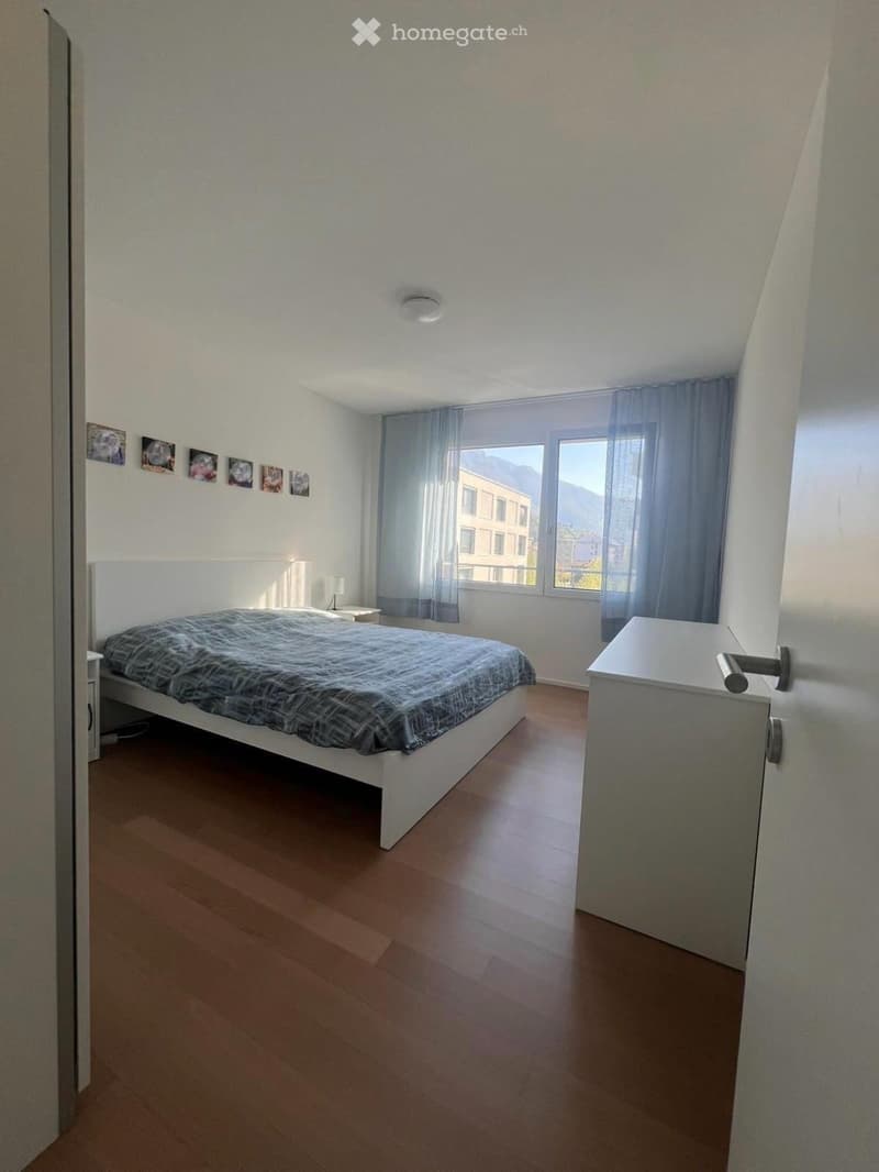 Bedroom with bed, nightstands, lamp, and window with curtain. Wooden floor and white walls.