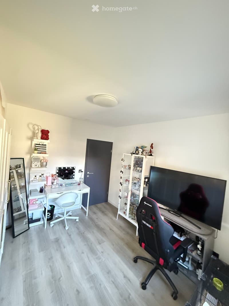 A room with a desk, chair, TV, cabinet, and mirror