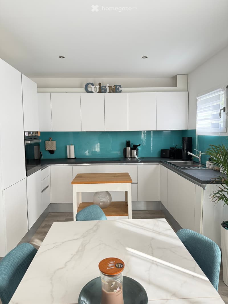 modern kitchen, white cabinets, teal backsplash, marble countertop, wooden table, blue chairs, sink, faucet, coffee maker, toaster, oven, countertop storage, potted plant