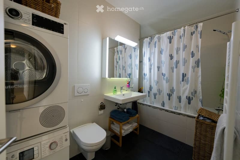 Bathroom with washing machine, sink, toilet, bathtub, shower curtain, towels, wicker basket, and wicker basket with towels.
