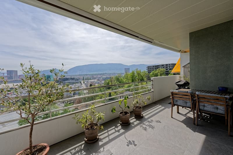 Balcony with table and chairs, potted plants, metal railing, city view