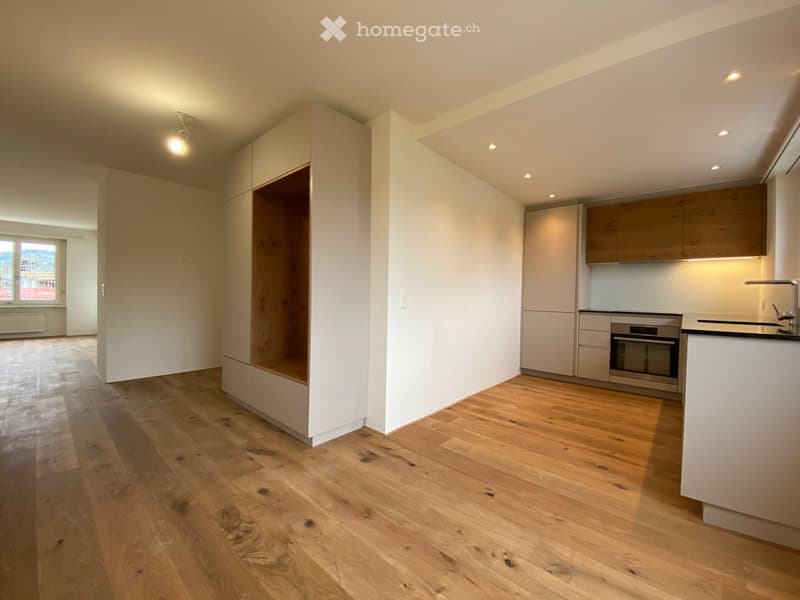 Empty room with wooden floor, white walls, built-in wardrobe, kitchen area with oven, sink, and cabinets