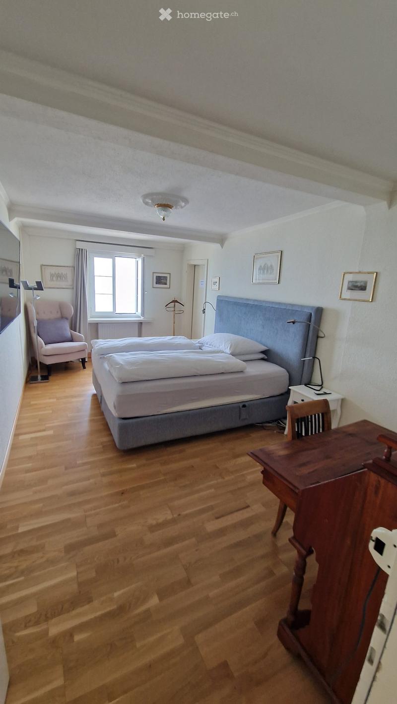 Bedroom with double bed, wooden floor, white walls, window, chair, desk, lamp, picture frames, radiator, ceiling lamp