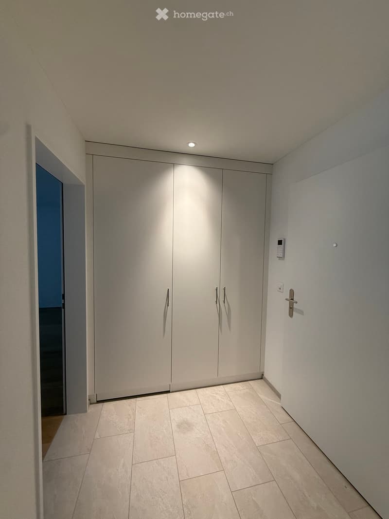 Empty room with white walls, tiled floor, large white wardrobe, door on the right, small door on the left