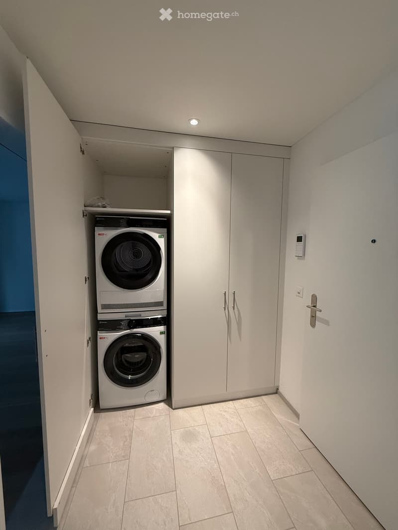 Laundry room with stacked washer and dryer, white cabinets, tiled floor, white walls