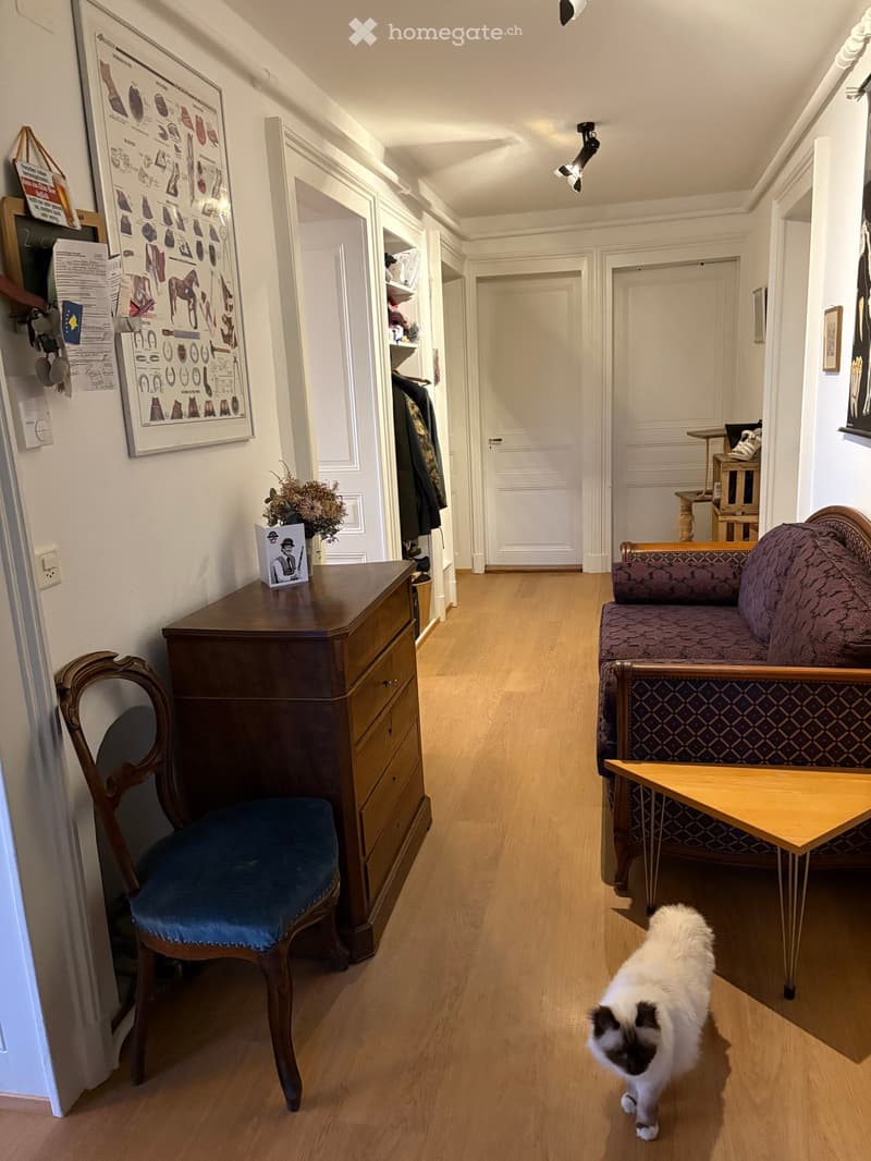 A room with wooden floor, a wooden chair, a wooden cabinet, a couch, a wooden table, a cat, and a picture frame on the wall.