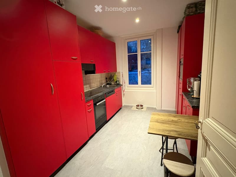 modern kitchen with red cabinets, black countertops, wooden table, black oven, sink, window