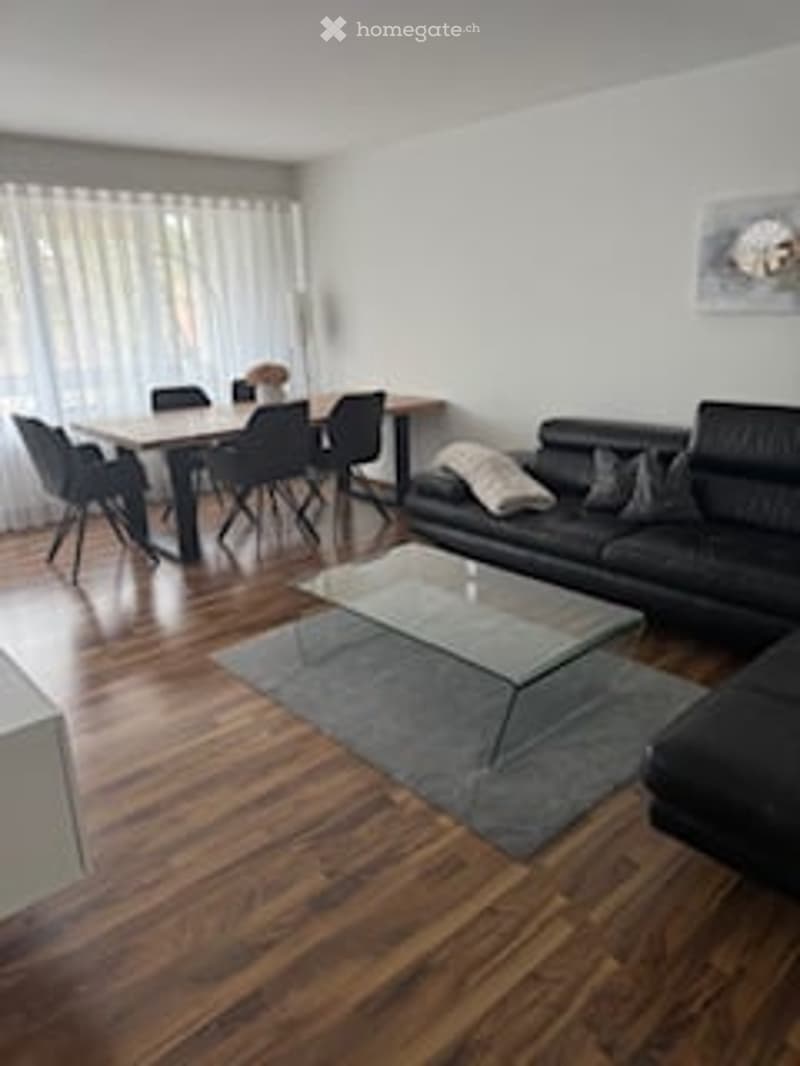 Living room with black leather couch, glass coffee table, wooden floor, dining table, chairs, white curtains