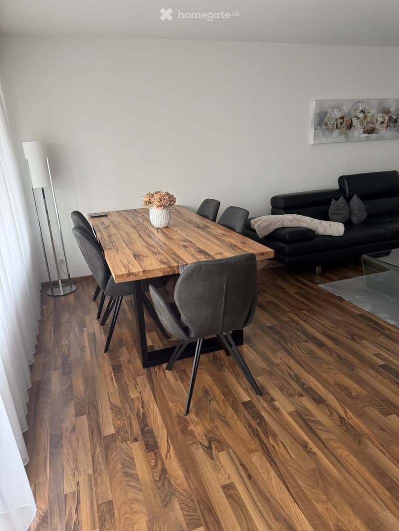 Dining room with wooden table, gray chairs, black couch, white curtains, floor lamp, picture frame