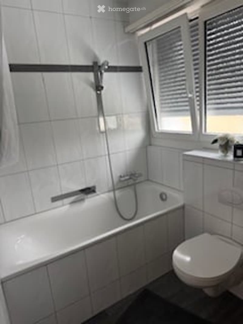 Bathroom with bathtub, toilet, white tiles, window with blinds, shower head