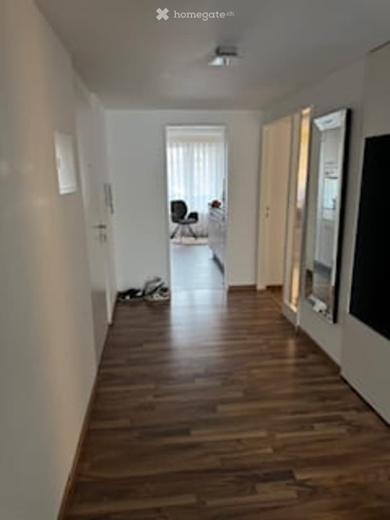 Empty hallway with wooden floor, white walls, and a mirror on the right side.