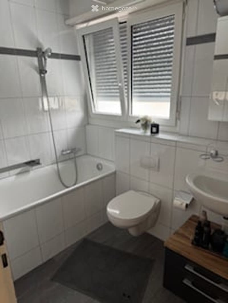 Bathroom with bathtub, toilet, sink, window with blinds, and a cabinet