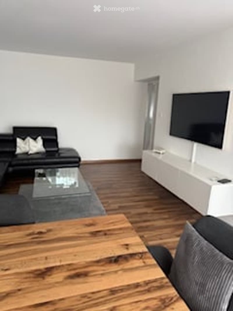 Living room with black leather sofa, glass coffee table, flat screen TV, white sideboard, wooden floor