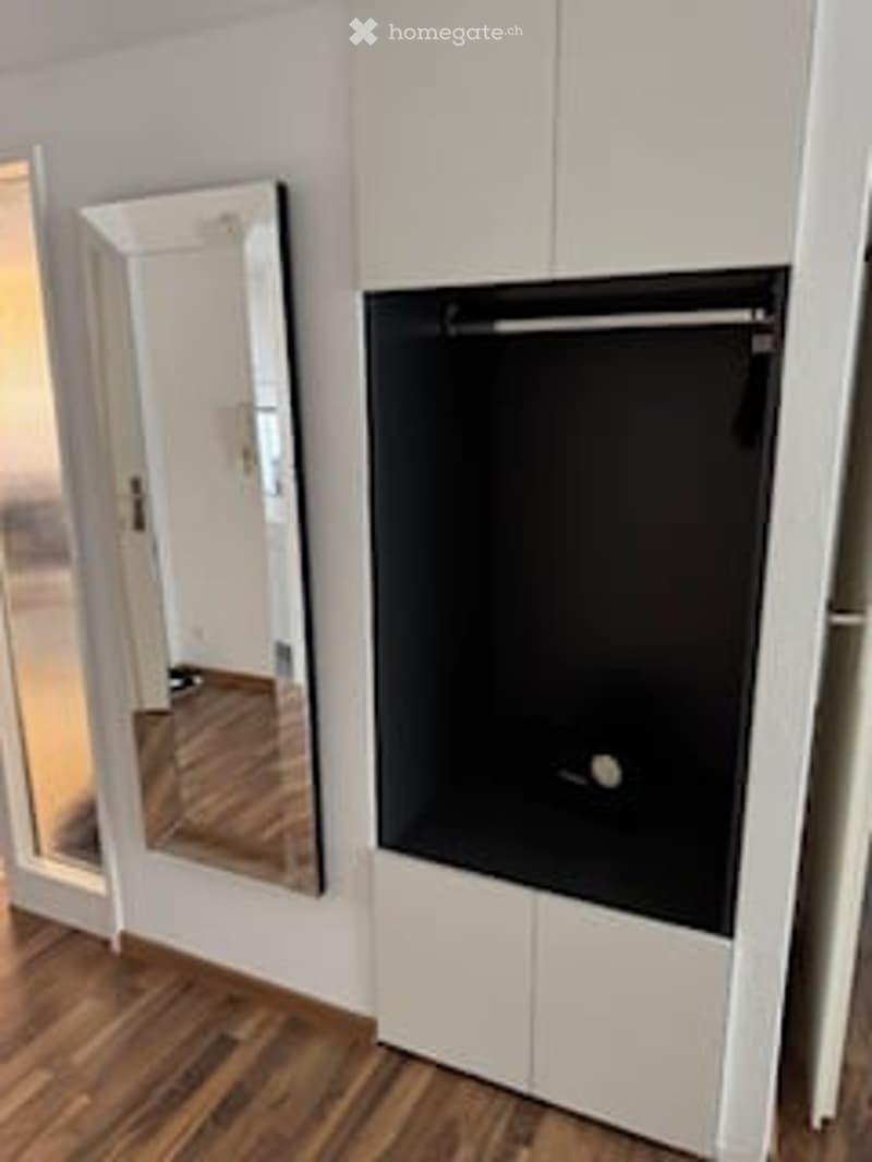 Empty room with wooden floor, white wardrobe, mirror, and open closet