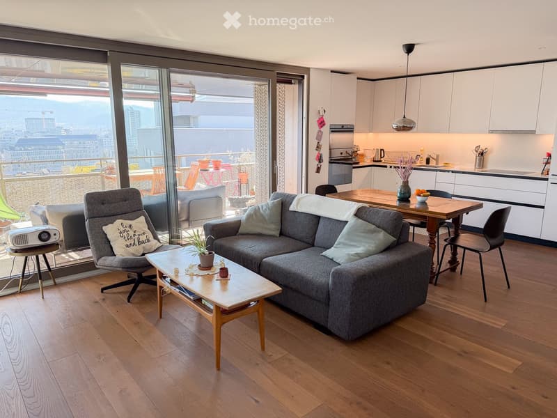 modern living room, large windows, balcony, gray couch, wooden coffee table, wooden dining table, kitchen area, white cabinets, modern kitchen appliances