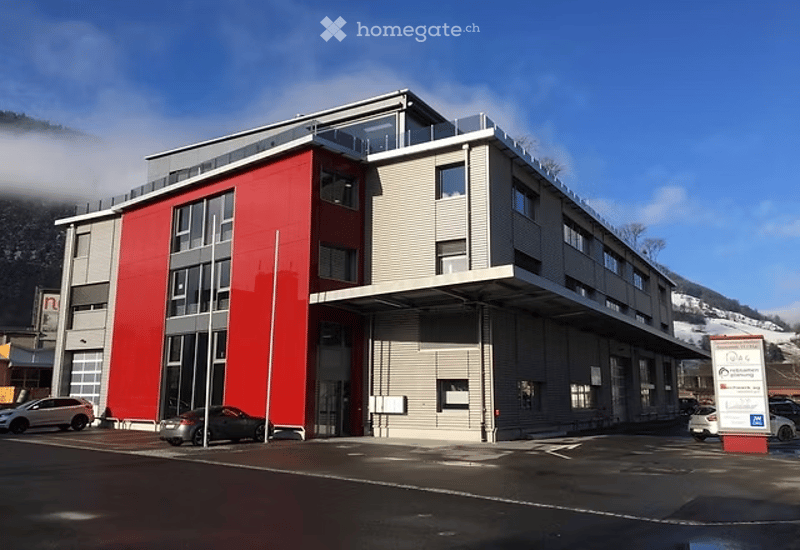 3 story building, red and gray exterior, multiple windows, cars parked in front