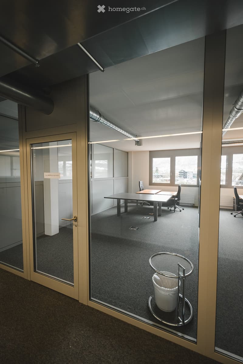 empty office room with glass walls, tables, chairs, trash bin, carpeted floor, windows