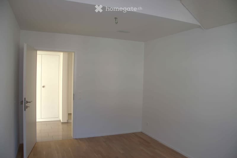 Empty room, wooden floors, white walls, open door to another room, small hallway, light fixtures