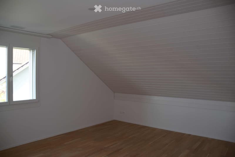empty attic room with sloping ceiling, wooden floor, white walls, window