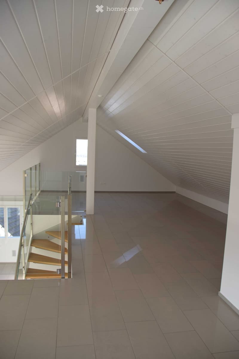 A room with beige tiled floor, glass wall, wooden staircase, and white paneling.