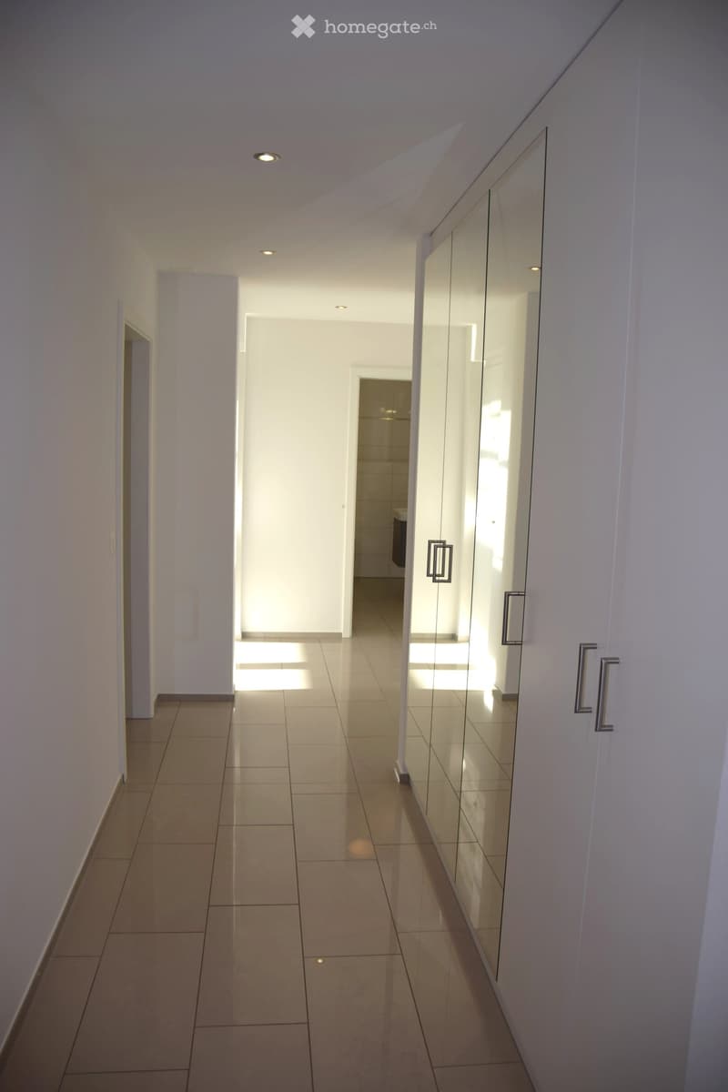 Long hallway with tiled floor, recessed ceiling lights, glass wall mirror, doors on both sides