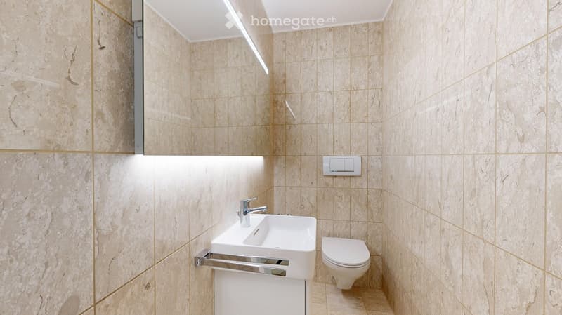 Bathroom with white sink, mirror, toilet, and beige tiles