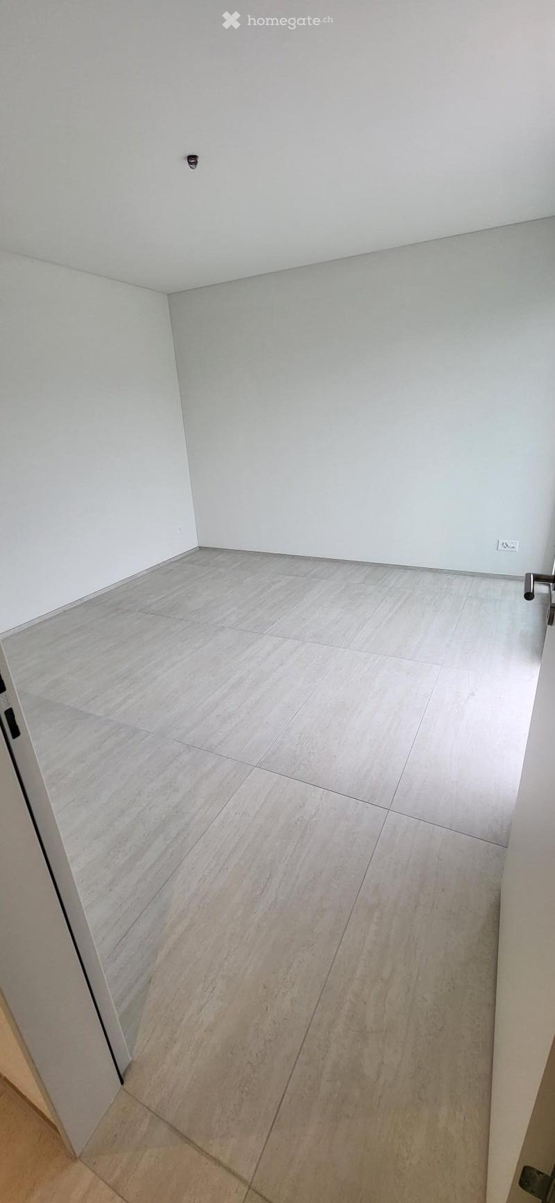 Empty room with white walls, tiled floor, and an open door.