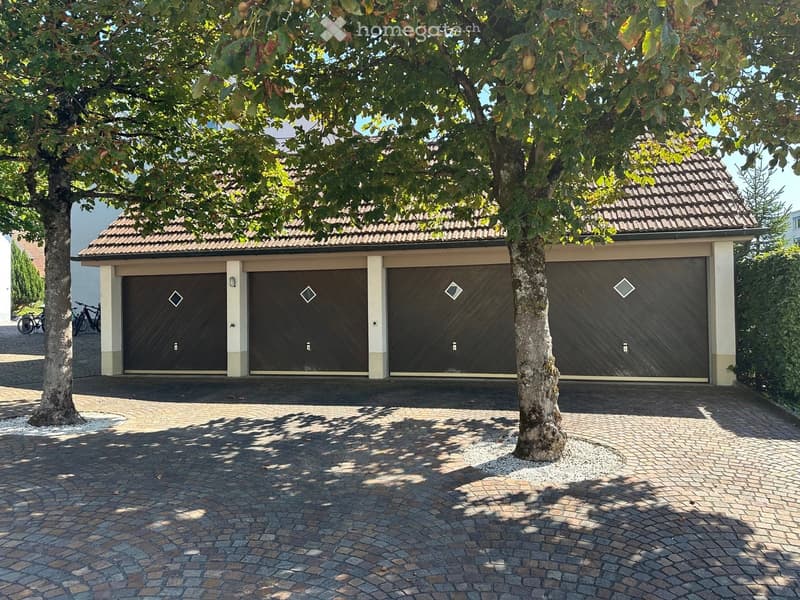 Garage with three doors, brick walls, brown roof, paved driveway, trees