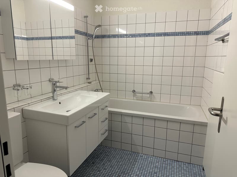 Bathroom with white tiles, bathtub, sink, toilet, shower head, and mirror.