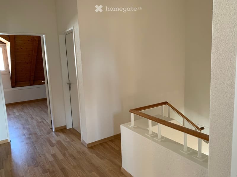 Empty room with wooden floor, white walls, wooden handrail, open door, wooden ceiling