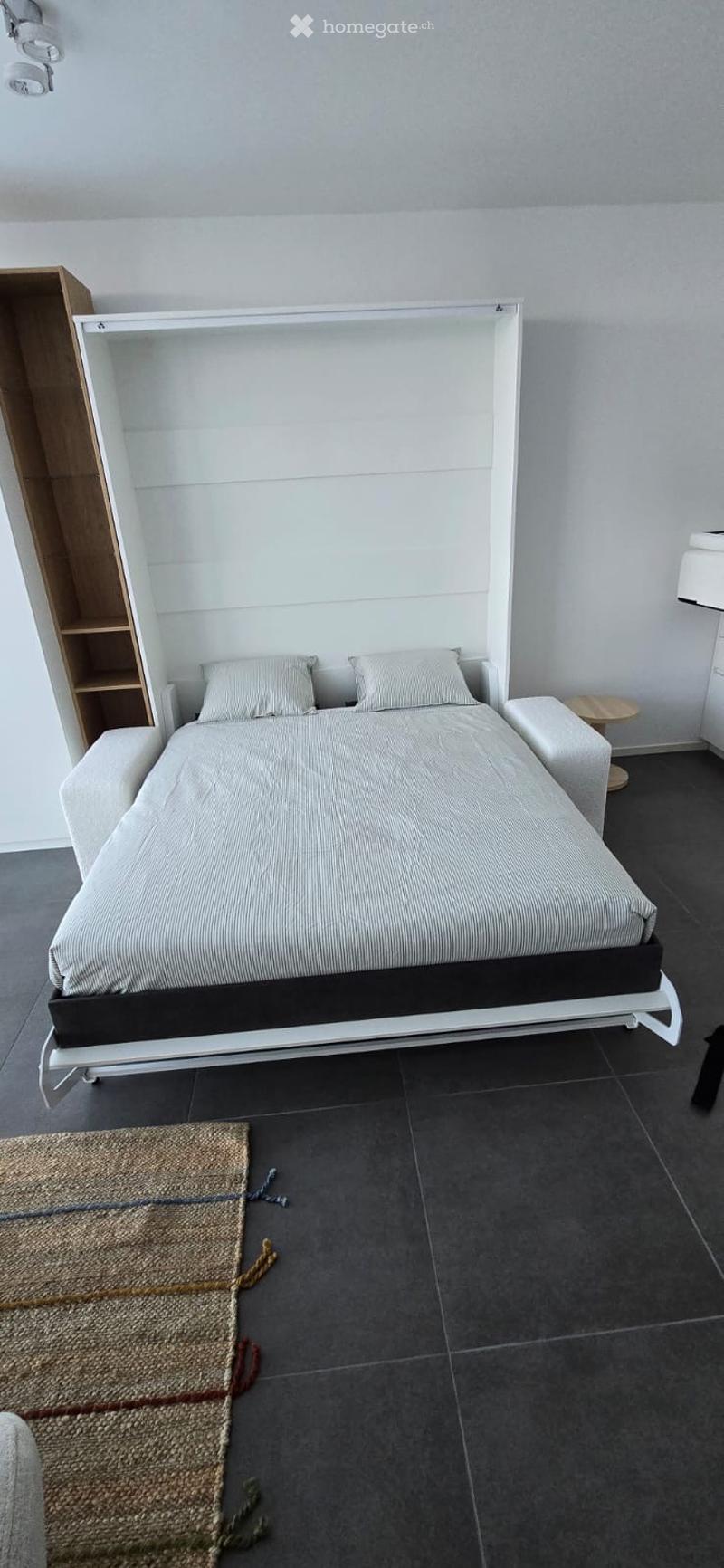 white convertible bed with storage compartments, white bedside tables, brown rug, tall wooden cupboard
