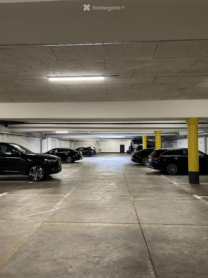 underground parking lot with several cars parked, yellow pillars, white ceiling, white walls, white floor
